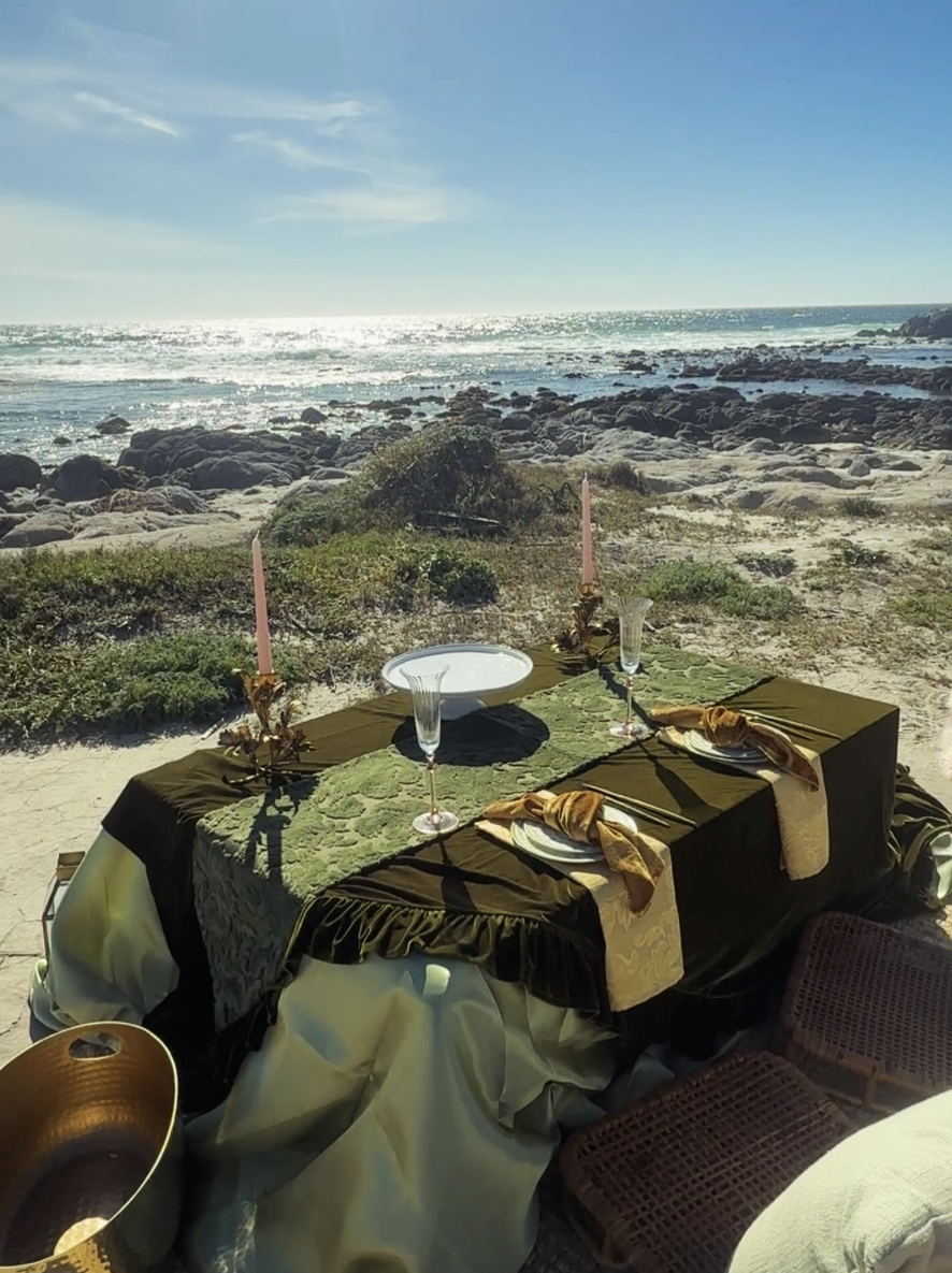Olive velvet tablescape with taper candles and gold napkin ties overlooking the surf