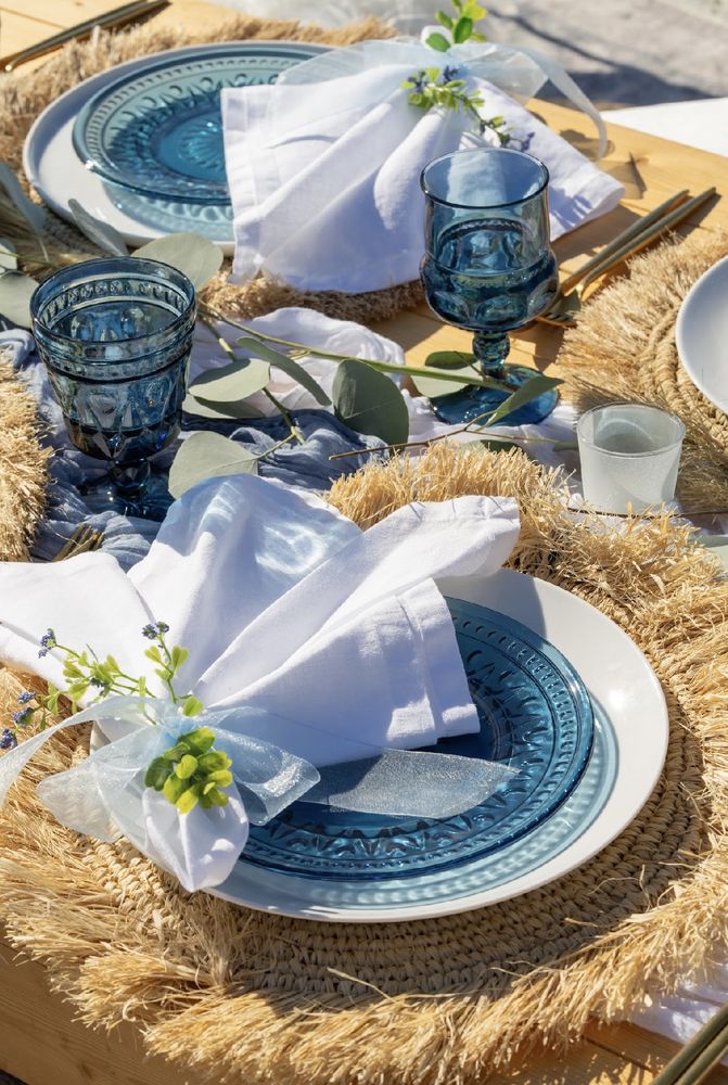 Close up place setting with blue pressed glass, white linen napkins and eucalyptus