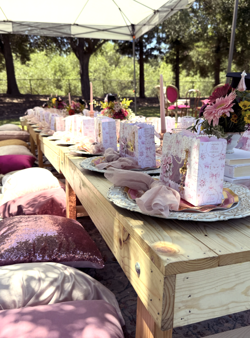 Long graduation picnic table with pink florals, favor boxes and satin floor pillows