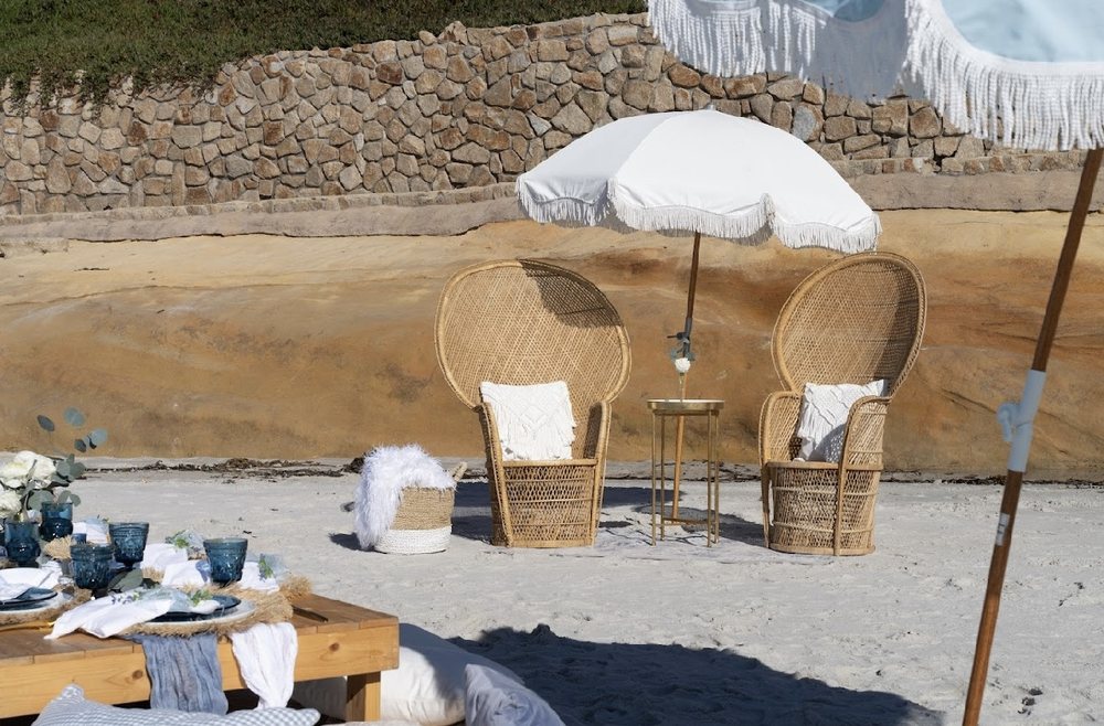 Rattan chairs, gold side table and fringed umbrella against a sandstone cove wall