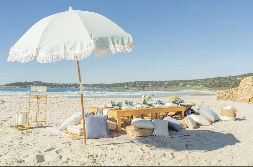 Seafoam fringed umbrella over a low beach table with pillows and floor cushions